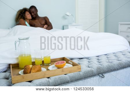 Romantic couple cuddling with breakfast tray on bed in bedroom