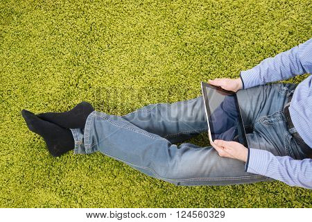 young man sitting on a green carpet with tablet
