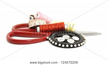 Sewing items: buttons colorful fabrics scissors measuring tape thimble spools of thread on sewing pattern