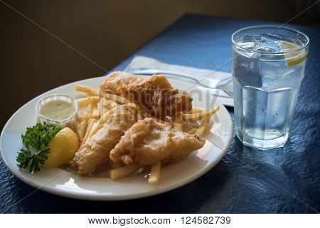 A Plate Of Fried Fish Cod Or Hallibut With French Fries Or Chips With A Glass Ow Water