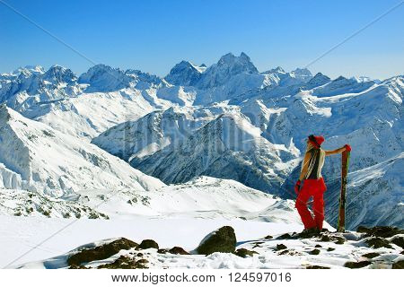 Skier wooman standing and viewing on the snowy mountains peaks and enjoy sunny day