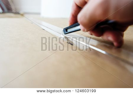 Man cutting with sharp cutter knife a cardboard box to open it before installing furniture