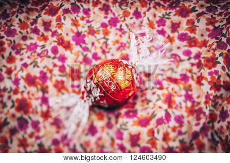 KILCHBERG SWITZERLAND - MARCH 20 2014: Lindt Lindor chocolate truffle on a red luxury floral background. Lindt is one one of the lastgest luxury chocolate and confectionery company worldwide with more than 30 factories worldwide
