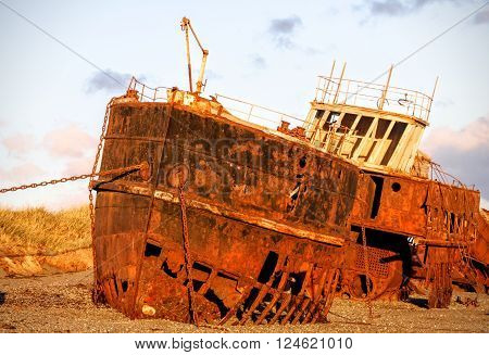 Rusted ship wrecked on beach at sunset with purple clouds.