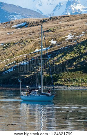White sloop motoring past fields and mountains