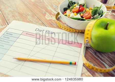 healthy eating, dieting, slimming and weigh loss concept - close up of diet plan paper green apple, measuring tape and salad