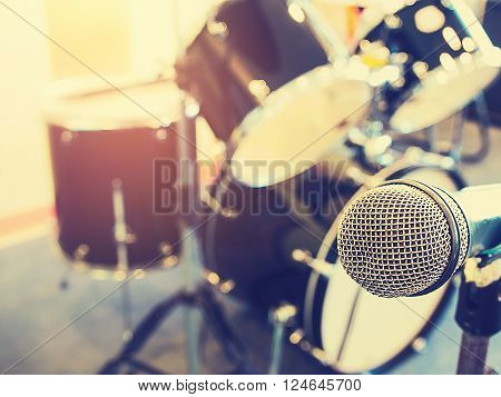 Microphone in in a recording studio or concert hall with drum in out of focus background. Vintage style and filtered process.