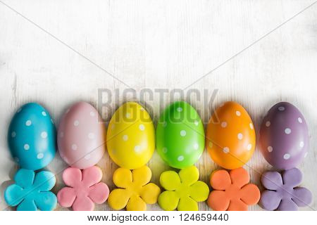 Colorful easter eggs and homemade fondant covered flower cookies on a white wood background