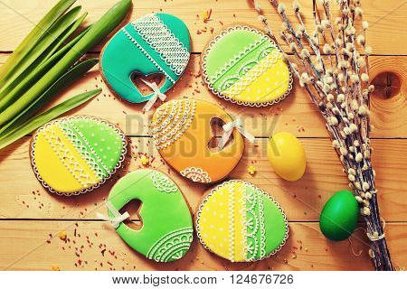 Easter homemade gingerbread cookie and yellow end green eggs over wooden table. Colorful toned image top view