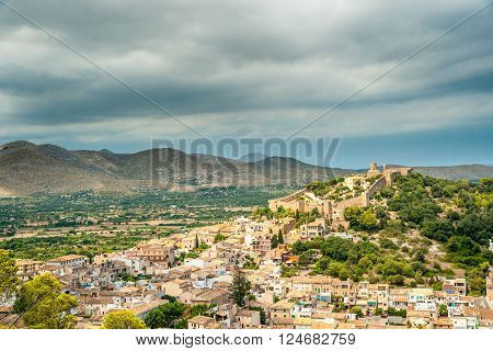Capdepera castle on green hill in Mallorca island, Spain. Beautiful landsacape with medieval architecture, green trees and blue sky with clouds on a sunny day.