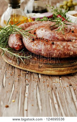 raw beef sausages on a cast-iron pan with rosemary and spices on a wooden table South African boerewors