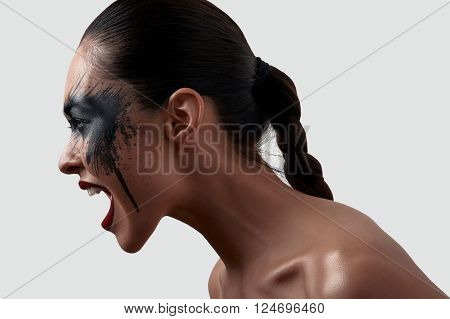 Screaming Female Model with opened Mouth and black Paint on her Face. American Indian Halloween Makeup Art