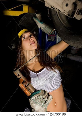 Beautiful young female mechanic inspecting car in auto repair shop. Girl welder is prepared to connect parts. Sexy mechanic.