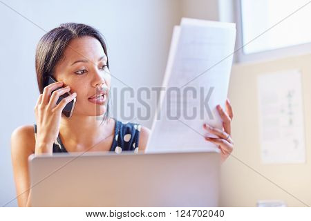 A young businesswoman talking on the phone while looking at a document