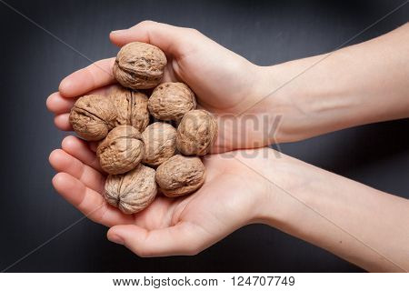 hands holding handful of walnuts over wooden table. view from the top