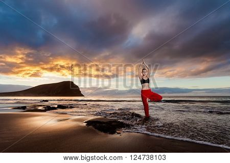 Summer sunrise yoga session on beautiful Playa de La Tejita beach with view on atlantic ocean and Punta Roja rock - tropical Tenerife island Canary in Spain. Vriksha-asana tree pose