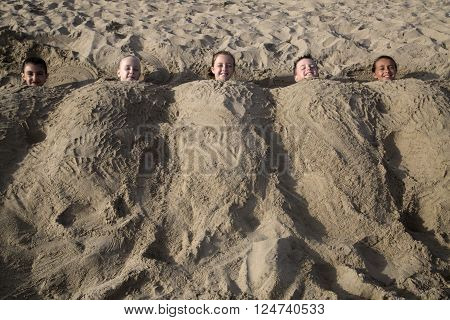 Five cute happy caucasian children buried in the sand on the beach