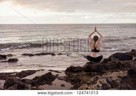 Summer sunrise yoga session on beautiful Playa de La Tejita beach with view on atlantic ocean and Punta Roja rock - tropical Tenerife island Canary in Spain. Meditation - lotus pose - padma asana