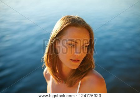 Portrait of a young beautiful girl in sunset light, with water in the background
