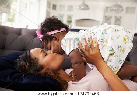 Mother reclining, holding and kissing her toddler daughter