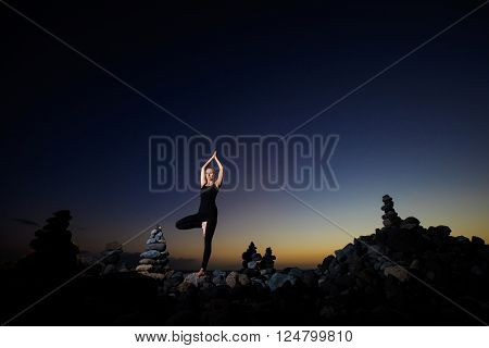 Summer sunset yoga session on beautiful Playa del Duque beach with stone pile stacks silhouettes - tropical Tenerife island Canary in Spain. Vriksha-asana tree pose