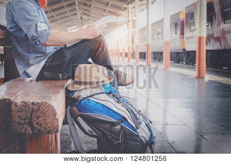 Side portrait of a young man traveler sitting with map choose where to travel and bag waiting for train vintage tone filter effected