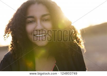 Beautiful happy mixed race African American girl teenager female young woman with perfect teeth smiling in golden light with sun flare at sunset or sunrise
