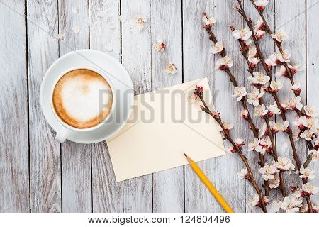 A cup of coffee next to the spring white flowers on wooden texture. Space for text.