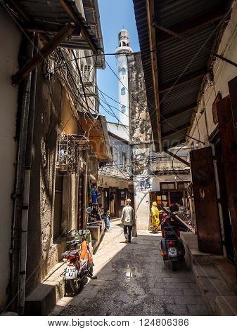 STONE TOWN ZANZIBAR - MAY 02 2015: One of the narrow streets in the old part of Stone Town Zanzibar in East Africa. Vertical orientation wide angle. Mosque's minaret in the background.