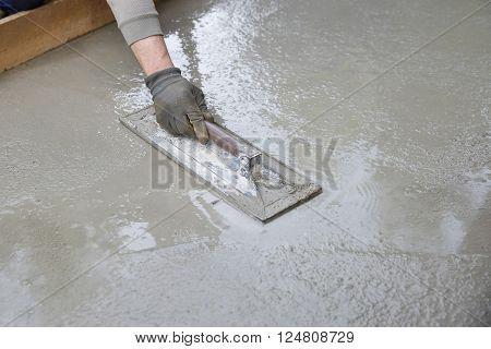 Mason leveling and screeding concrete floor base with square trowel in front of the house. Construction business, do-it-yourself, precision work around the house concept.