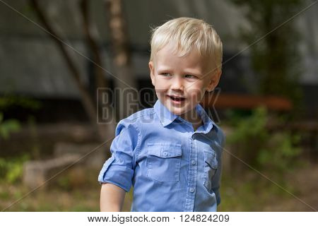 Portrait of blonde baby boy in summer street, outdoors
