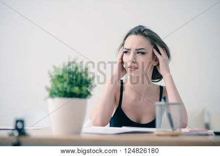 Many tasks to do. Tired pleasant attractive woman touching her head and feeling tired while sitting at  the table