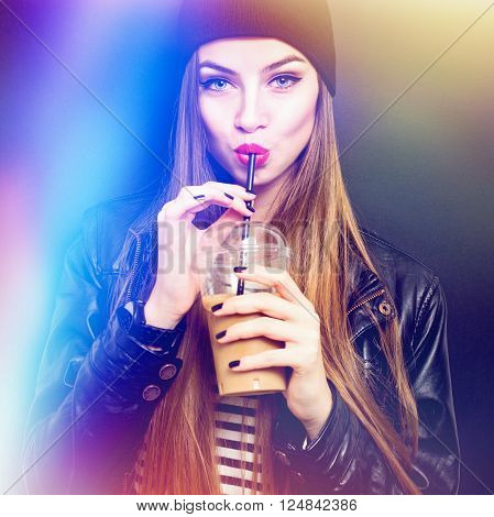 Cool blonde teenage girl in black drinking takeaway coffee from plastic cup with straw.