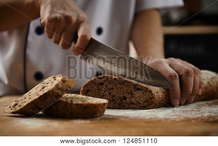 Woman chef cutting healthy bread with seeds on wooden board. Bakehouse. Bread production.