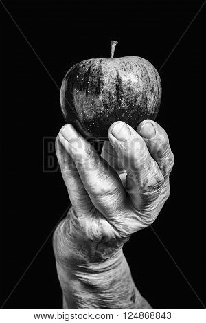 Old hand holding an apple on black background