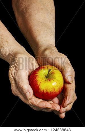 Old hands holding an apple on black background