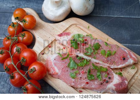 Pork slices with spices and herbs with a branch of cherry tomatoes and mushrooms