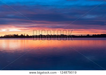 Sky color reflections in calm bay Tauranga sunrise of amazing intensity portends changing weather ahead.