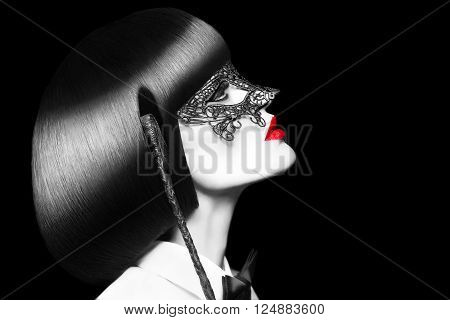 Sexy woman in mask holding whip at night, selective coloring. BDSM. Mask and tux outfit with red lips and cleopatra hair style.