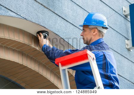 Male Technician Installing Camera Standing On Stepladder