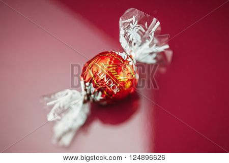 KILCHBERG SWITZERLAND - MARCH 20 2014: Lindt Lindor chocolate truffle on a red luxury silk background. Lindt is one one of the lastgest luxury chocolate and confectionery company worldwide with more than 30 factories worldwide