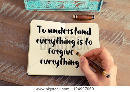 Retro effect and toned image of a woman hand writing on a notebook. Handwritten quote To understand everything is to forgive everything as inspirational concept image