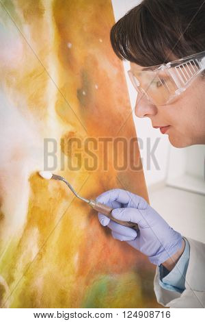 Artwork conservator at work with old painting wearing protective suit