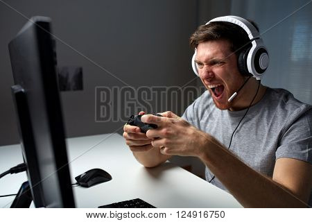 technology, gaming, entertainment, play and people concept - angry screaming young man in headset with controller gamepad playing computer game at home and streaming playthrough or walkthrough video