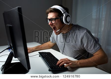 technology, gaming, entertainment, let's play and people concept - angry screaming young man in headset with pc computer playing game at home and streaming playthrough or walkthrough video
