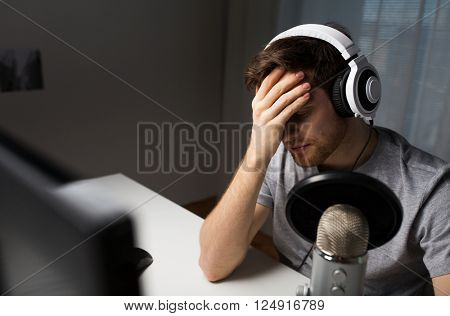 technology, gaming, entertainment, let's play and people concept - close up of sad young man in headset with pc computer playing game at home and streaming playthrough or walkthrough video