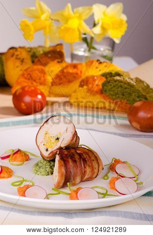Chicken fillet wrapped in bacon stuffed with cheese on a plate with vegetables Easter bread in the background