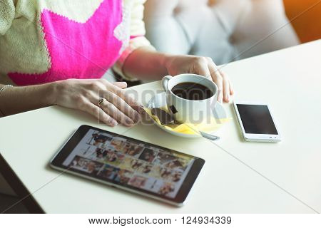 Female hand on the table, technology, internet, woman drinking coffee using the tablet and phone looking photos in social networks.