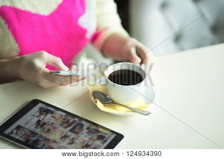 Female hand on the table looking in the phone message, technology, internet, woman drinking coffee and using a tablet looks pictures on social networks.