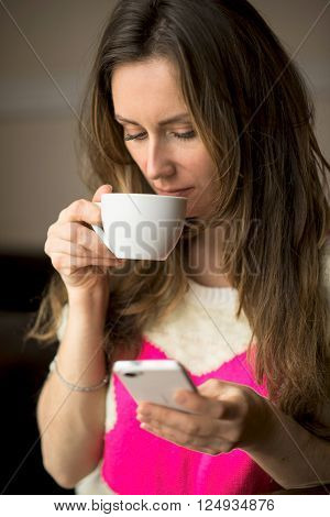 Young girl holding a cup of hot coffee or tea sitting in the cafe and writes or reads a message on the phone, lifestyle, breakfast or lunch, healthy lifestyle, fashion, in a yellow sweater.